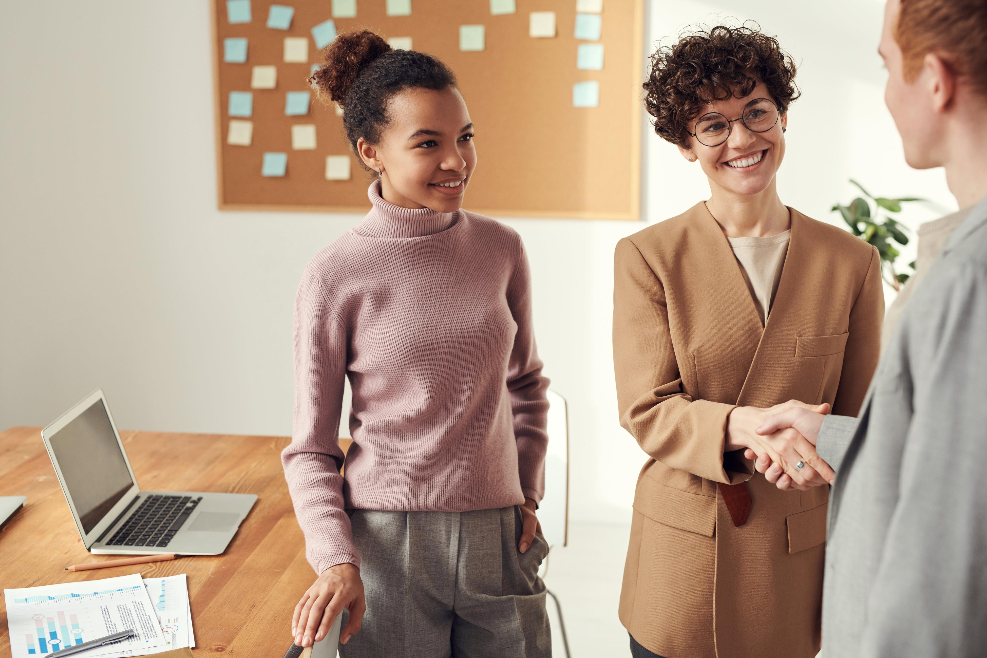 Three people meeting. Two are shaking hands.