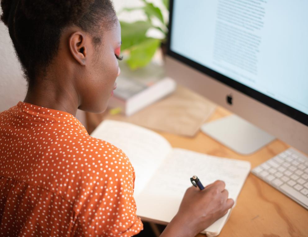 A woman is shown writing in front of her computer.